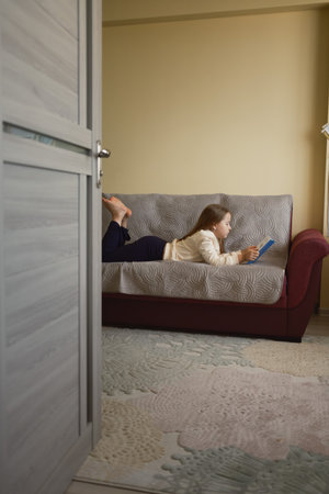 Child reading a book on a cozy sofa in a quiet roomの写真素材