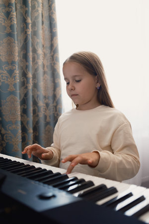 Young girl playing electronic keyboard near a window with patterned curtains