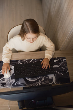 Young girl using computer at wooden desk for learning or web browsingの写真素材