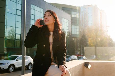Professional woman making a phone call outside modern office building at daytimeの写真素材