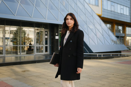 Stylish young professional woman standing confidently near a modern building exteriorの写真素材