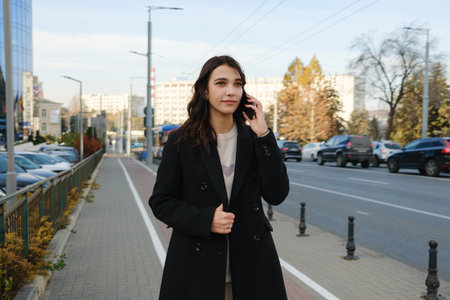 Woman talking on phone outdoors while walking along a busy city sidewalkの写真素材