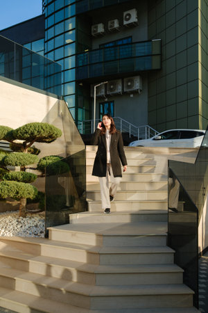 Businesswoman walking down outdoor steps while talking on a smartphoneの写真素材