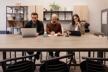 Three people in a collaborative workspace engaged in group discussion and note-taking
