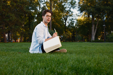 Young man writing in a notebook sitting in a green parkの写真素材