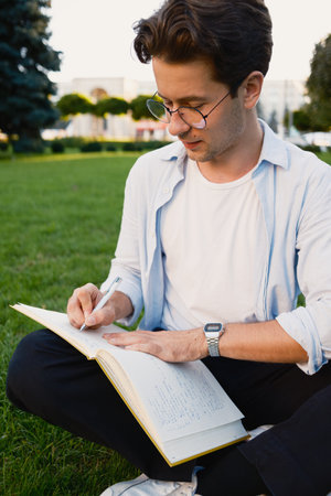 Young man writing in a journal outdoors on a sunny dayの写真素材
