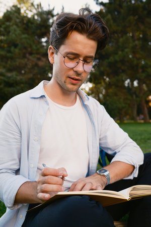 Young man writing in notebook outdoors in a peaceful green parkの写真素材