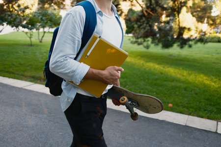 Student carrying skateboard and notebook in a park on a sunny day