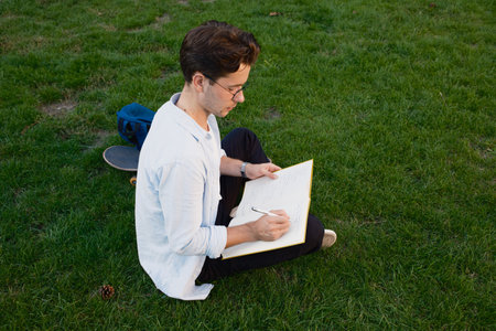 Man writing in a notebook while sitting outside on the grassの写真素材