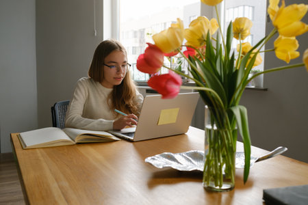 Teenage girl studying at home with laptop and books on a sunny day