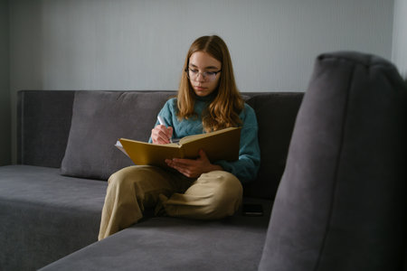 Teenage girl studying while sitting comfortably on a sofa in a cozy room