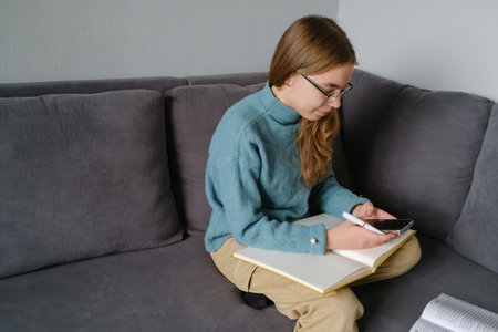 Teenage girl studying at home using her smartphone and notebookの写真素材