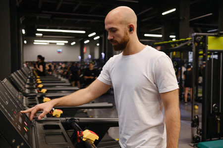 Bald man using treadmill in modern gym environment with fitness equipmentの写真素材