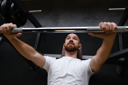 Man performing weightlifting bench press exercise in a modern gym environmentの写真素材