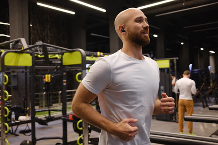 Smiling man jogging on a treadmill in a modern fitness gym