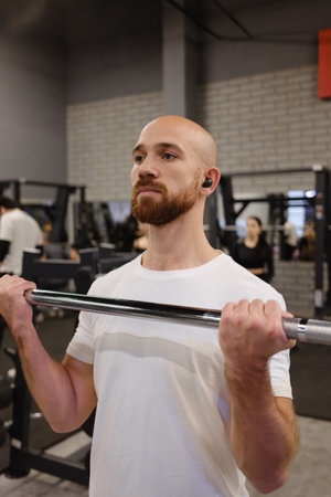 Man lifting barbell in a gym wearing white shirt and listening to music