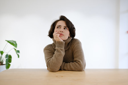 Woman in a sweater sitting thoughtfully at a wooden table