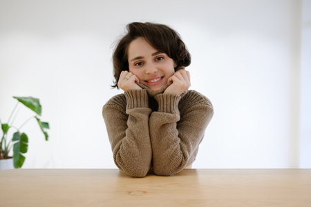 Smiling woman in warm cozy sweater with leaning hands, plant in backgroundの写真素材