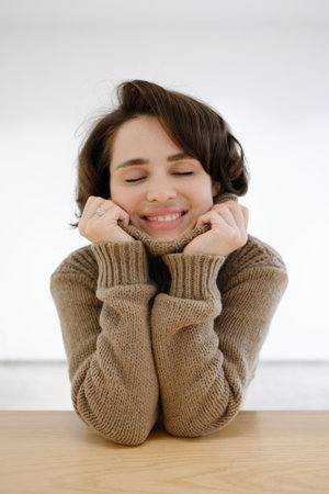 Smiling woman enjoying cozy moment wearing a warm sweater at a wooden tableの写真素材