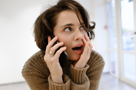 Woman surprised while engaged in a phone conversation in a modern settingの写真素材