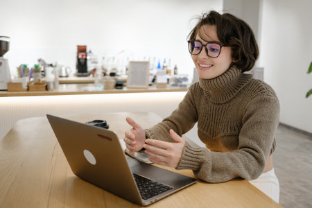Young woman video conferencing on her laptop in a cozy cafe settingの写真素材