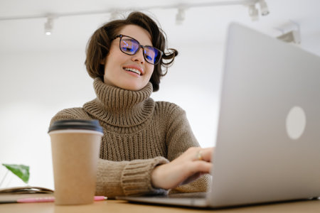 Young woman smiling while working on a laptop in modern workspaceの写真素材