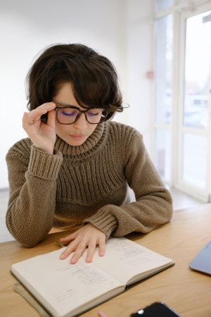 Woman reading a notebook at a desk in a cozy indoor settingの写真素材