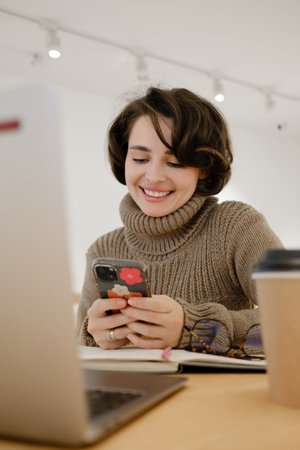 Smiling woman using smartphone and working at a cafe with coffee and laptopの写真素材