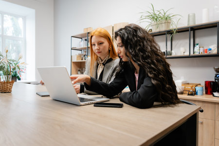 Two women collaborate on a laptop at a bright modern workspace sharing ideas