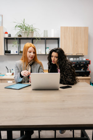 Two women collaborate at a laptop in a modern studio, planning togetherの写真素材