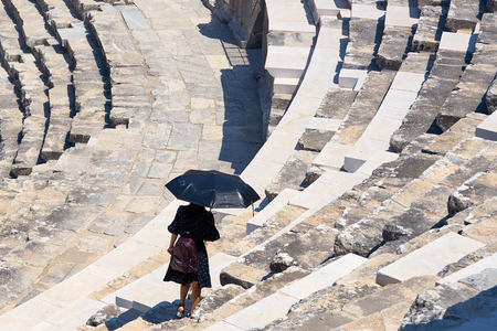 A Woman under black umbrella walking on ancient rock stairs on a hot sunny day.の写真素材