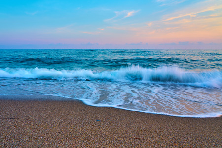 Sunset at the beach, waves with foam hitting sand.の写真素材