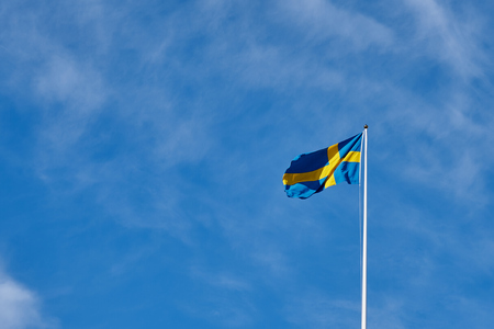Flag of Sweden against a blue cloudy sky on a background. Copy space for text.の写真素材