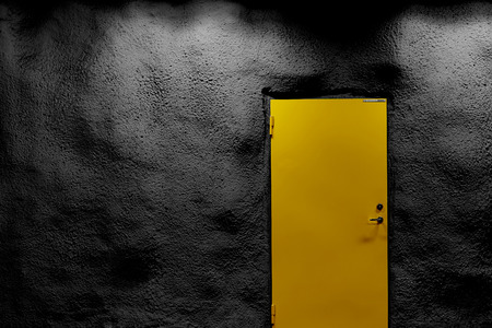 Yellow door with black wall with shadows and light. Copy space.の写真素材