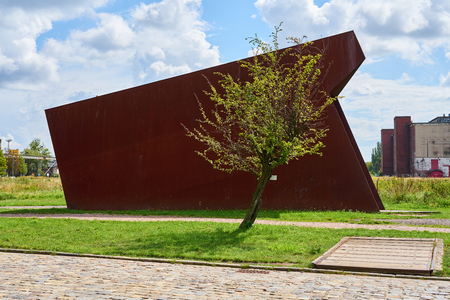 Lonely tree in sunlight with rusty metal on a background under a blue cloudy sky near the Solidarity Square in Gdansk, Poland.の写真素材