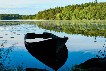 An old boat silhouette on a lake coast. Reflections of trees and sky in water.の写真素材