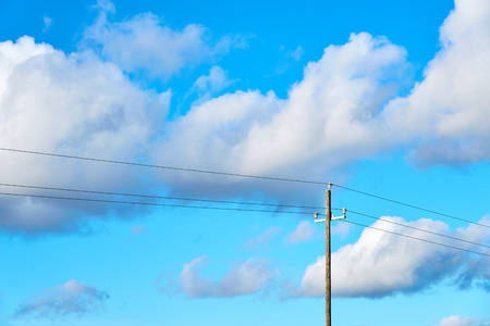 Wooden electric pole against a blue cloudy sky.