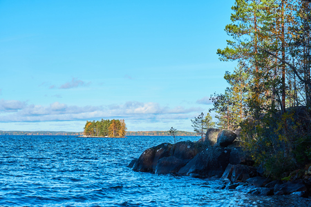 Coast of a lake with blue water, trees and granite stones. Colorful island with autumn colors on a background. Copy space.の写真素材