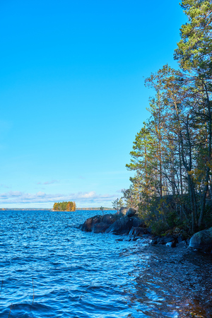 Coast of a lake with blue water, trees and granite stones. Colorful island with autumn colors on a background. Copy space.の写真素材