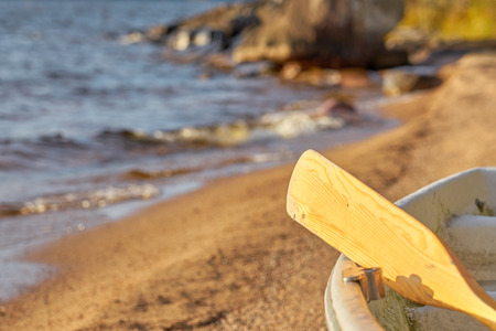 A wooden paddle on a boat on a sandy beach with a blurred lake shore on a background.の写真素材
