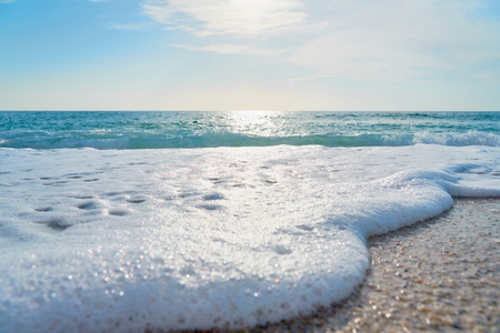 White foam close up on sandy beach with waves as a natural background with reflection of sunlight on water. Summer holiday concept.の写真素材