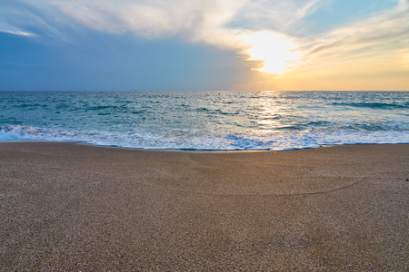 Sunset at the tropical beach, sun behind clouds reflects on water and waves with foam hitting sand.の写真素材