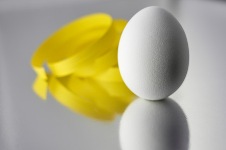 A white egg with yellow ribbon on a silver reflective background. Easter concept. Copy space.