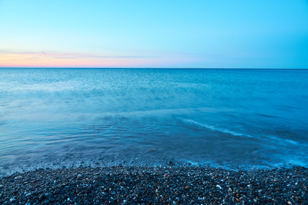 Pebble beach on a sunset with blurred seawater and horizon on a background. Copy space.の写真素材
