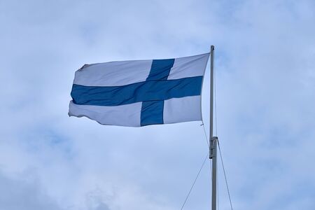 Flag of Finland outdoors against a blue sky with clouds.の写真素材
