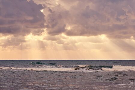Sun rays behind the huge cloud over waving water on tropical sea coast on a sunset.の写真素材