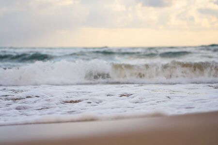 Sandy beach on a sunset with reflection on wet sand and waves with foam. Copy space.