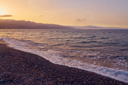 Waves on a pebble beach on a sunset. Natural background.