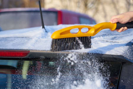 Clearing snow from the roof of a car with a brush. Copy space.