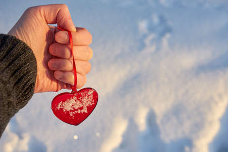 A red glass heart in the hand of a young white man with a blurred winter snow in the background. Valentines day concept.の写真素材